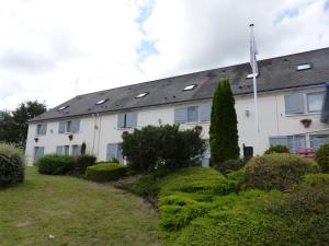 a white building with a roof with windows and bushes at The Originals City, Hôtel Alizéa, Le Mans Nord (Inter-Hotel) in Saint-Saturnin