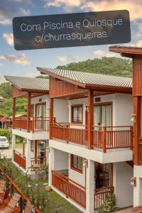 a house with wooden balconies and a sign that reads com piscina at Pousada Rosa Maria in Praia do Rosa