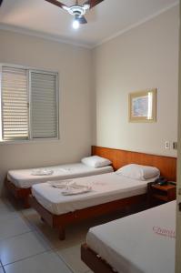 a room with three beds and a window at Hotel Chantilly in Presidente Prudente