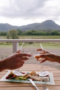 two people holding wine glasses in front of a plate of food at Leogate Estate Villas in Pokolbin