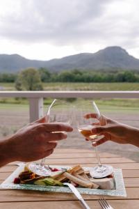 due persone che portano bicchieri di vino davanti a un piatto di cibo di Leogate Estate Villas a Pokolbin