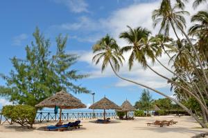 einen Strand mit Sonnenschirmen, Stühlen und Palmen in der Unterkunft Ocean Paradise Resort & Spa in Pwani Mchangani