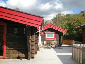 ein Blockhaus mit einer roten Markise sowie Tischen und Stühlen in der Unterkunft 9 person holiday home in H LLEVIKSSTRAND in Hälleviksstrand