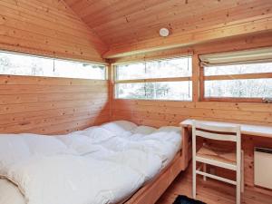 a bed in a log cabin with a desk and two windows at Holiday home Læsø III in Læsø