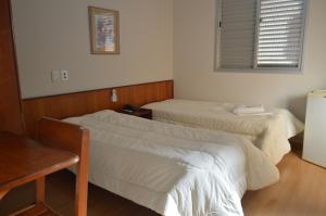 a room with two beds and a table and a window at Hotel Chantilly in Presidente Prudente