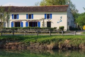 a house with blue and white windows next to a river at Le logis du héron in Coulon