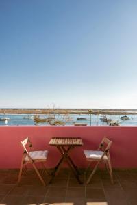 una mesa y dos sillas junto a una pared roja en Casa Viana - Guesthouse, en Cabanas de Tavira