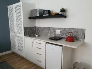uma cozinha com armários brancos e uma chaleira de chá vermelho em Plett57 - Self Catering - Room No1 em Plettenberg Bay