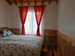 1 dormitorio con 1 cama con cortinas rojas y ventana en Hotel Cochamó en Cochamó