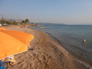 a beach with an orange umbrella and people in the water at Gina's Studios in Aliveri