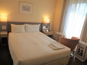 a hotel room with a large white bed and a chair at Hotel JAL City Nagano in Nagano