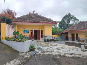 un edificio amarillo con un gran patio delante en Penginapan Mentorogo Kaliurang Mitra RedDoorz en Kaliurang