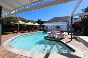 a swimming pool with tables and chairs and a house at 19th Hole Guest Lodge - Golfers paradise in Hermanus