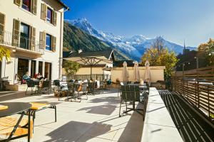 un patio con mesas y sillas con montañas en el fondo en Cosmiques Hotel - Centre Chamonix en Chamonix-Mont-Blanc