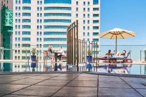 eine Gruppe von Menschen, die um einen Pool mit einem Regenschirm sitzen in der Unterkunft Carlton Dubai Creek Hotel in Dubai