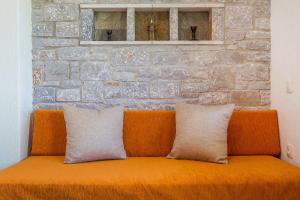 スタフィオスにあるIrida Apartmentsの煉瓦の壁に枕2つ付きのオレンジカウチ