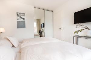 a white bedroom with a bed and a flat screen tv at Kapitänshaus Roseney in Norderney