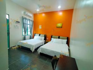 um quarto com 2 camas e uma parede laranja em anjung ara suites and roomstays em Kuala Terengganu