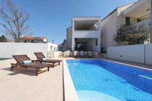 a swimming pool with two chairs next to a house at Corte villas & apartments - AE1043 in Privlaka