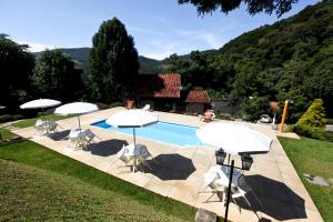 une piscine avec des parasols et des chaises ainsi qu'une maison dans l'établissement Pousada Alpes, à Santo Antônio do Pinhal