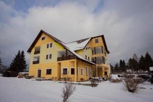 una gran casa amarilla con nieve en el techo en Pensiunea Valurile Bistritei en Vatra Dornei