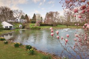 een vijver in een tuin met een huis en roze bloemen bij The Inn at Whitewing Farm in West Chester