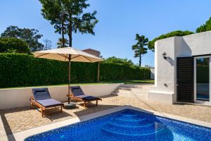 un patio con 2 sillas y una sombrilla junto a la piscina en Villa do Pinhal en Olhos de Água