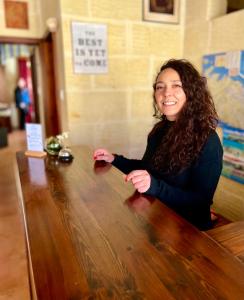 una mujer sentada en una mesa de madera sonriendo en Grotto's Paradise B&B en Għarb