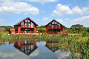 two wooden houses sitting next to a body of water at Swallow Lodge with Hot Tub, dogs welcome sleeps 8, Great resort Facilities in Padstow