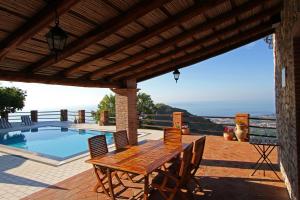 een houten tafel en stoelen op een patio met een zwembad bij Villa Etna Mare - Pool villa in peaceful location with breathtaking views of the sea, Mt Etna & Taormina - in Taormina