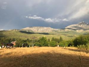a field with mountains in the background and a house in the foreground at El Bolsón Patagonia - Cabaña Tío Ale in El Bolsón