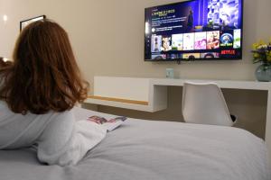 Una donna seduta su un letto che guarda la TV di Alma Suites a Napoli