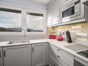 eine Küche mit weißen Schränken und einer Spüle und einem Fenster in der Unterkunft Manesty View in Keswick