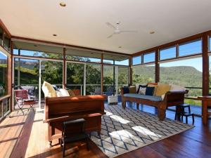 a living room with glass windows and a piano at Budderoo Unique with 270 degree views in Upper Kangaroo River