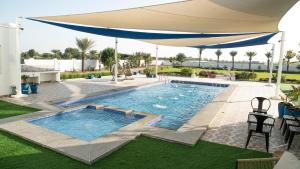 a swimming pool with an umbrella on a lawn at Luxury Farm Villa in Musanaa Oman in Al-Musannah