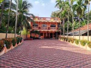 a large orange building with palm trees and a brick driveway at Nallur Holidays Inn in Jaffna