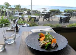 a plate of food on a table with a view of the ocean at Hôtel & Restaurant LES MOUETTES - Larmor Plage, Proche de LORIENT in Larmor-Plage