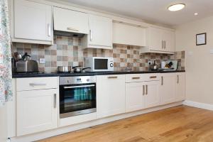 una cucina con mobili bianchi e un forno a microonde di Low Croft Cottage a Grasmere Altre 4 foto