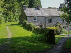 ein altes Steinhaus auf einer grasbewachsenen Straße in der Unterkunft Coachmans Cottage in Levens