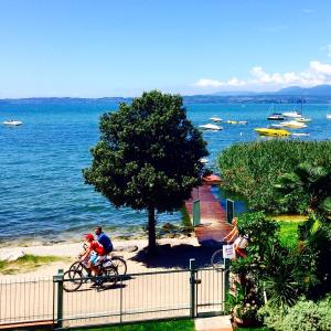 un hombre y una mujer montando una bicicleta junto al océano en Hotel Campagnola, en Bardolino