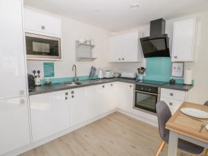 a kitchen with white cabinets and a wooden table at Hafan Traeth Beach Haven in Benllech