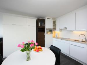 a white kitchen with a table with a vase of flowers at Studio Studio met garage by Interhome in Bredene