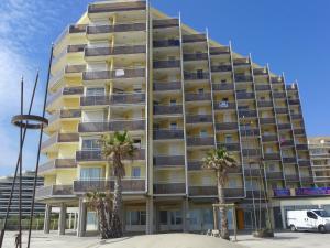 a tall yellow building with palm trees in front of it at Apartment Le Beach-24 by Interhome in Canet-en-Roussillon