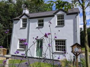 ein weißes Haus mit lila Blumen davor in der Unterkunft Riverside cottage walking distance into Caernarfon in Caernarfon