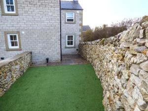 a stone wall next to a house with a green yard at 3 Primitive Croft in Chelmorton