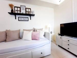 a white bedroom with a couch and a tv at 1 BR Cozy Farmhouse-Style Condo with Balcony & Taal View at Wind Residences in Tagaytay