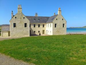 a large stone building on the side of a grass field at Balnakeil House in Balnakeil
