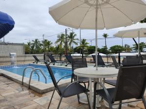 un tavolo e sedie con ombrellone accanto a una piscina di Praia Hotel Enseada a Maceió