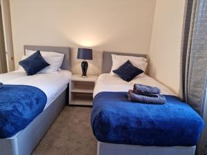 1 dormitorio con 2 camas con sábanas azules y reposapiés azul en Two Bedroom Penicuik Apartment, en Penicuik