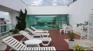 a deck with white chairs and a swimming pool at Guarujá Flat in Guarujá